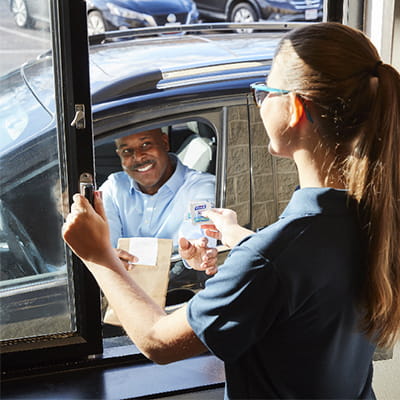 Drive-through restaurant worker hands drive-up customer a PURELL hand sanitizing wipe
