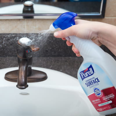 Someone spraying restroom sink with PURELL surface disinfectant