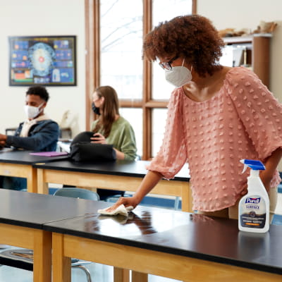Professor cleaning desk in college classroom with PURELL surface disinfectant spray