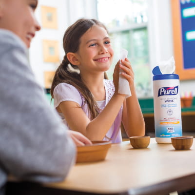 Elementary aged girl using PURELL hand sanitizing wipes at classroom table with friends