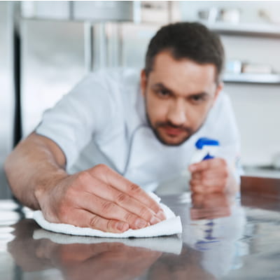 Young male professional cook cleaning surface in commercial kitchen