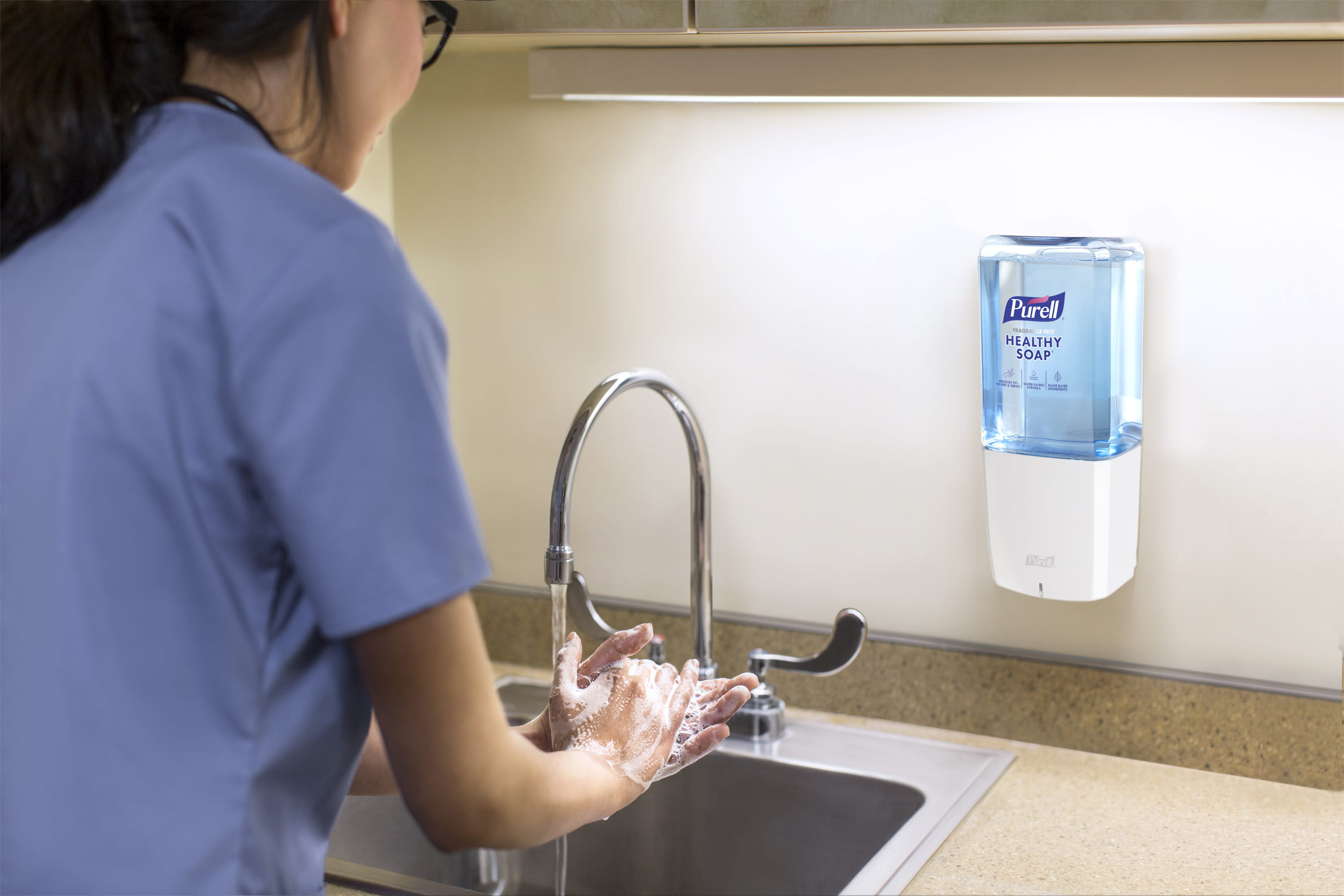 A person washes thier hands at a sink with a mounted PURELLL ES10 dispenser and Heathy Soap.