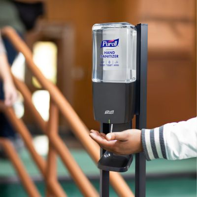 A person uses a PURELL dispenser to get hand sanitizer after use a stair railing.