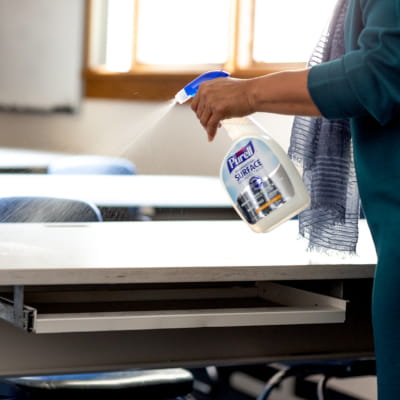 Teacher cleaning desk with PURELL Surface Spray