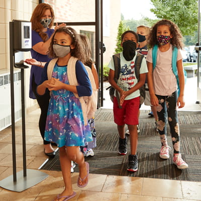 Children walking into school lobby, using PURELL hand sanitizer dispenser