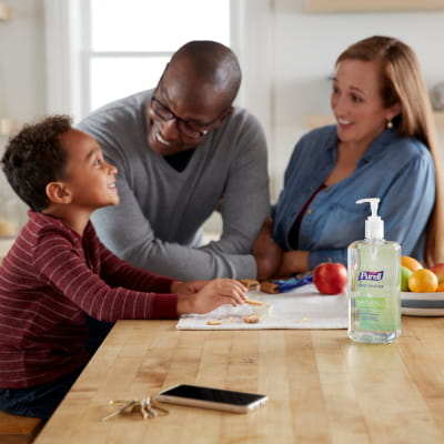 Boy having a snack at a kitchen counter with PURELL hand sanitizer next to them while talking to mom and dad