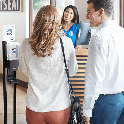guests speaking with a concierge at the front desk with a purell hand sanitizer stand in view