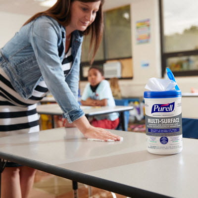A teacher wiping down a table with PURELL Surface Wipes